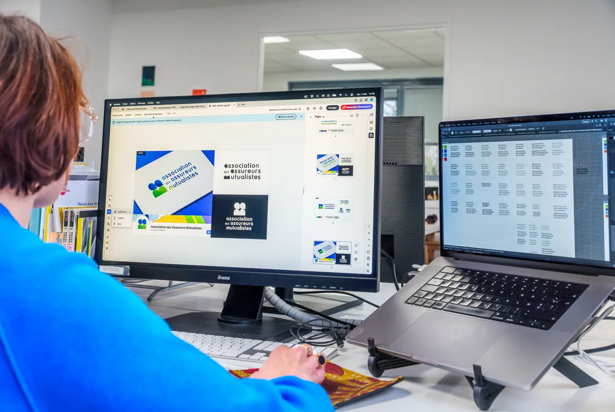 Graphiste EcloLINK travaillant sur des propositions d'identité visuelle pour un client, avec déclinaisons de logos affichées à l'écran