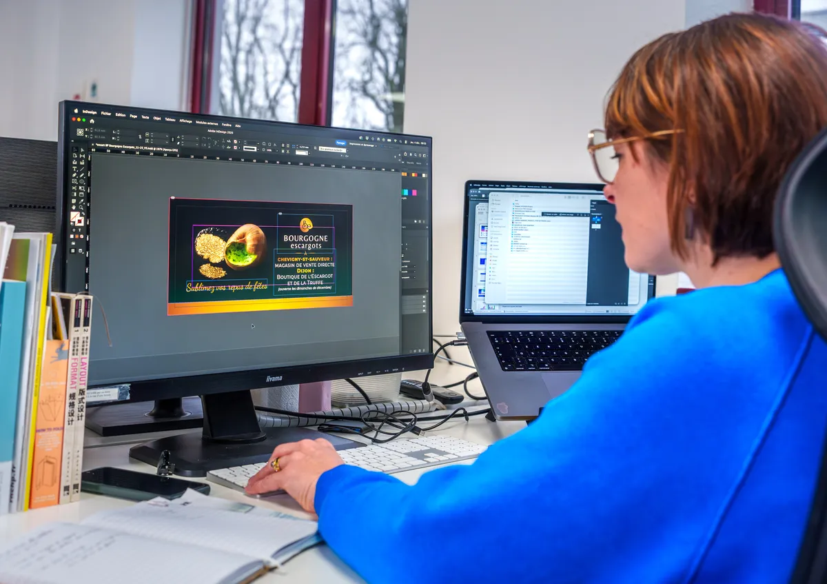 Graphiste EcloLINK de profil travaillant sur un visuel promotionnel sous Adobe InDesign