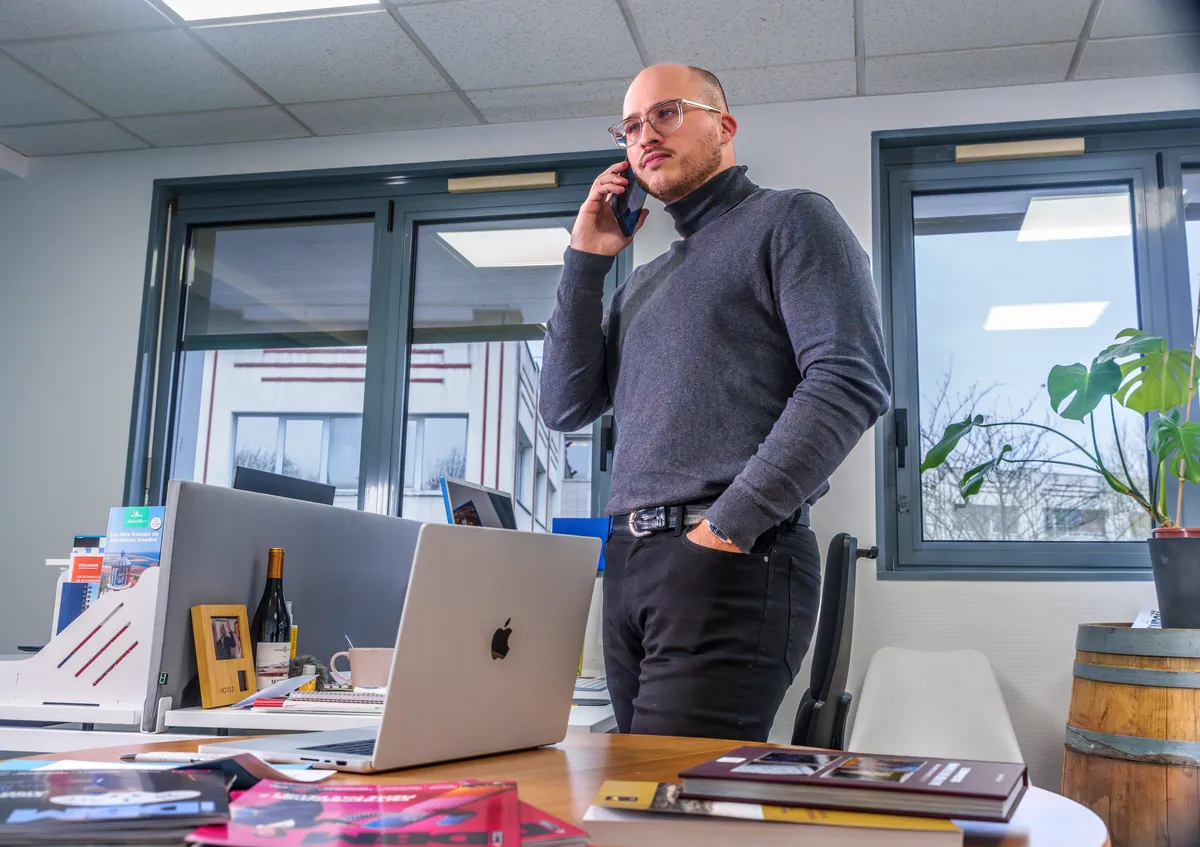 Directeur commercial EcloLINK en conversation téléphonique dans son bureau avec vue sur les locaux de l'agence