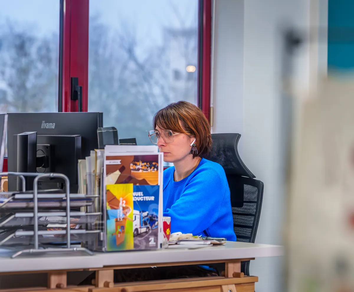 Collaboratrice travaillant sur ordinateur portable pendant qu’une collègue l’accompagne dans le bureau.