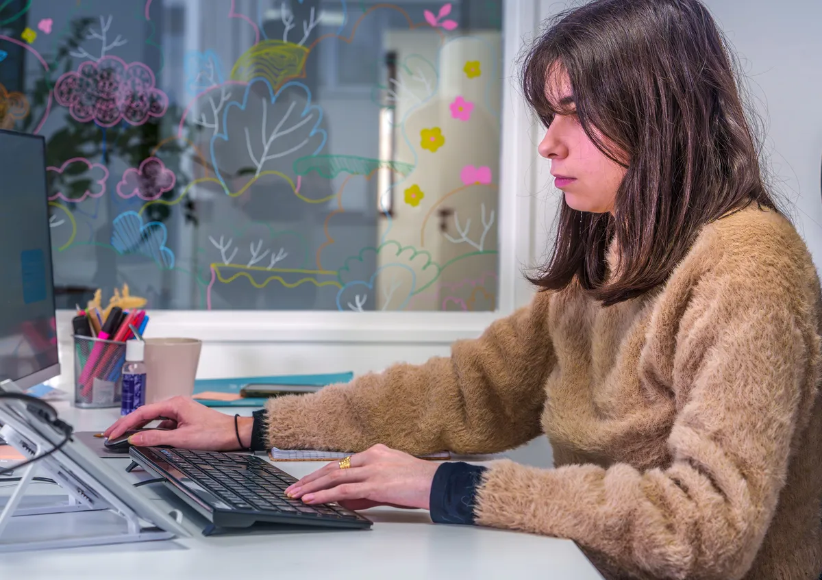 Collaboratrice travaillant au clavier dans un bureau avec mur vitré décoré de dessins colorés.